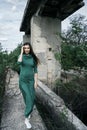 Lovely girl in green dress and with loose hair goes through the old stone bridge in the out of town.