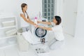 Lovely girl helps mum with washing, stands in basket, gives bottle of detergent or washing powder , woman stands on knees, loads Royalty Free Stock Photo