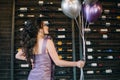 Lovely girl holding her birthday balloons in front of decorative wine bottles