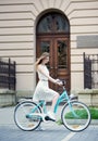 Lovely girl in light dress and sneakers on blue retro bike against the background of an old building Royalty Free Stock Photo