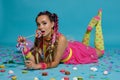 Lovely girl with a multi-colored braids hairstyle and bright make-up, posing in studio with lollipop, air balloons and