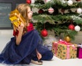 Lovely Girl Sitting on Floor in Front of Christmas Tree with Gift Box. Royalty Free Stock Photo