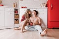 Lovely girl sitting on the floor and having fun with boyfriend. Young couple enjoying coffee or tea in the kitchen Royalty Free Stock Photo