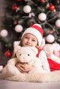 Lovely girl sitting on the floor near the Christmas tree with a bear, studio shot, toning in vintage style. Royalty Free Stock Photo