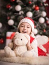 Lovely girl sitting on the floor near the Christmas tree with a bear, studio shot, toning in vintage style. Royalty Free Stock Photo