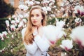 Lovely girl standing near Magnolia blossoming flowers, stands in white pink dress a small smile smiling Royalty Free Stock Photo