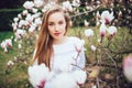 Lovely girl standing near Magnolia blossoming flowers, stands in white pink dress a small smile smiling Royalty Free Stock Photo