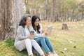 Lovely granddaughter and grandmother sitting under the tree in the green park together, watching video on tablet Royalty Free Stock Photo