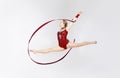 Charming gymnast with string doing split leap in the air on white background