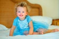 Lovely happy blonde toddler girl sitting on a bed