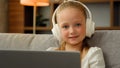 Lovely happy child pretty girl in headphones sit at apartment listen music on laptop playing computer games funny little Royalty Free Stock Photo