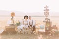 The lovely horizontal portrait of the vintage dressed newlyweds sitting with the dogs on the sofa surrounded with the