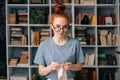 Lovely joyful redhead young woman wearing casual glasses is knitting handmade clothes with spokes.