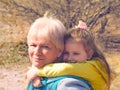 Lovely kid girl hangs on grandmother neck  hugs her from behind piggybacking and laughing together. Hugs and joy with grandma Royalty Free Stock Photo