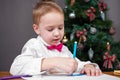 Lovely kid in white shirt with bow tie is writing letter with wishes to Santa or painting greeting card for parents to