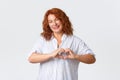 Lovely and kind, smiling redhead middle-aged woman showing heart gesture, express sympathy or care, love and charish Royalty Free Stock Photo