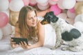 Lovely lady in pajama making selfie in her bedroom using phone and hug her dog. Indoor portrait  girl with baloons in morning. Royalty Free Stock Photo