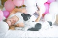 Lovely lady in pajama making selfie in her bedroom using phone and hug her dog. Indoor portrait  girl with baloons in morning. Royalty Free Stock Photo