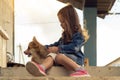 Lovely little girl caress pretty corgi dog sitting outdoors on floor in house yard, from below view. Doggy licking face.