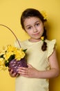 Lovely little girl with flowers in pigtail, dressed in yellow clothes, holding purple wicker basket with yellow roses