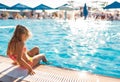 A lovely little girl sits on the side of the pool with her feet in the water enjoying the sun Royalty Free Stock Photo