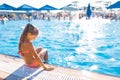 A lovely little girl sits on the side of the pool with her feet in the water enjoying the sun Royalty Free Stock Photo