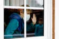 Lovely little school kid boy by a window wearing medical mask at home or school during pandemic coronavirus quarantine Royalty Free Stock Photo