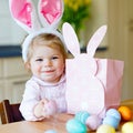 Lovely little toddler girl wearing Easter bunny ears playing with colored pastel eggs. Happy baby child unpacking gifts Royalty Free Stock Photo