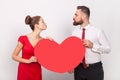 Lovely man and woman standing together, sending air kisses to each other, holding big heart. Royalty Free Stock Photo