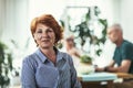 Middle-aged woman with smiling sitting on a chair at home looking at the camera with friends on background Royalty Free Stock Photo