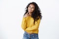 Lovely modern curly-haired female student in yellow sweater, tilt head silly and smiling camera, touch lip thoughtful