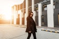 Lovely modern fashion model young woman in fashionable casual black dress in stylish sunglasses travels street at sunset. Lovely