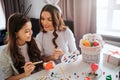 Lovely mother and daughter prepare for Easter. They paint eggs in room. Girl hold brush. Mother point on pallete