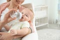 Lovely mother giving her baby drink from bottle in room. Royalty Free Stock Photo
