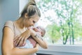 Lovely mother and infant relationship. Calm caucasian tattooed blonde girl in beige t-shirt holding her little baby boy Royalty Free Stock Photo