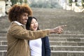 Lovely multiracial couple pointing to the right in a park.Two happy diverse young persons smiling and pointing with