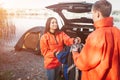 Lovely oyung woman in orange jacket looks at guy and takes backpack from him. she smiles. Young man looks at her. Thet