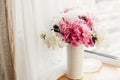 Lovely peony bouquet in sunny light on rustic wooden window sill. Stylish pink and white peonies in vase on wooden background.