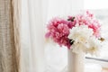 Lovely peony bouquet in sunny light on rustic wooden window sill. Stylish pink and white peonies in vase on wooden background.