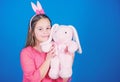 Lovely playful bunny child hugs soft toy. Bunny ears accessory. Bunny girl with cute toy on blue background. Child