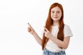 Lovely red head kid girl with freckles, ginger child pointing fingers at upper left corner, smile shy, standing over Royalty Free Stock Photo
