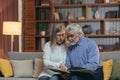 A lovely senior couple watching Memoirs photo album on sofa at home. Elderly family grandparents sitting together looking and Royalty Free Stock Photo