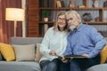 A lovely senior couple watching Memoirs photo album on sofa at home. Elderly family grandparents sitting together looking and Royalty Free Stock Photo