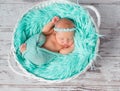 Lovely sleeping newborn girl in round cot with turquoise blanket