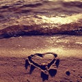 Lovely small heart sketched in salt sand at beach. Evening warm colors of sunset mirror in water level. Royalty Free Stock Photo