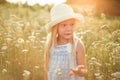 Lovely smiling blond girl in a field at sunset. Cute girl in a flowering field sniffs flowers. Ukrainian in a hat and dress near Royalty Free Stock Photo