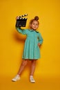 Lovely smiling little girl holding director's film movie slateboard over yellow studio background. Concept of human Royalty Free Stock Photo