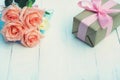 Lovely soft orange pink color rose tied by pink ribbon and brown gift box on white wood table background, sweet valentine present