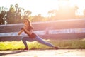 Lovely sporty woman stretching before workout at the stadium. Outdoor shot with sun rays. Space for text