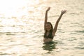 Lovely teen girl stay in the sea and express happiness during holiday with raise hands and wave also look at camera with warm Royalty Free Stock Photo